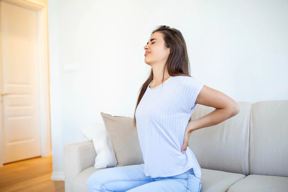 Woman sitting on the edge of a bed holding her lower back in pain
